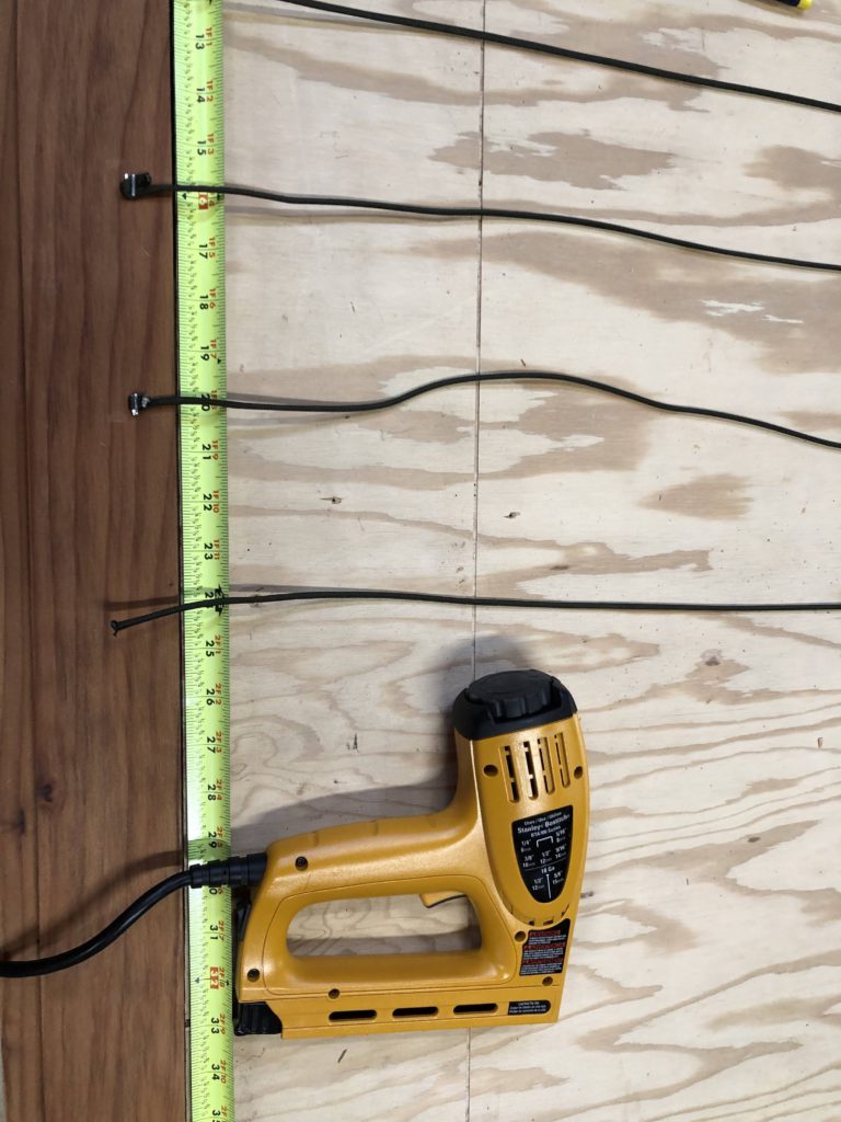 Staple gun lying next to an open tape measure, a board, and paracord strips.