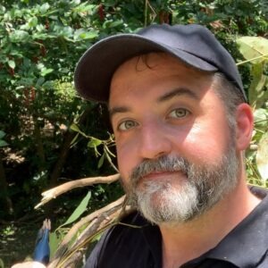 Joe_Cashmore2 Joe wearing a hat in front of bright green folage in a forest.